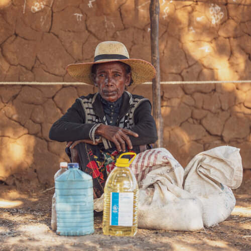 Ihminen istuu varjossa edessään WFP:n ruokaöljyä ja vettä