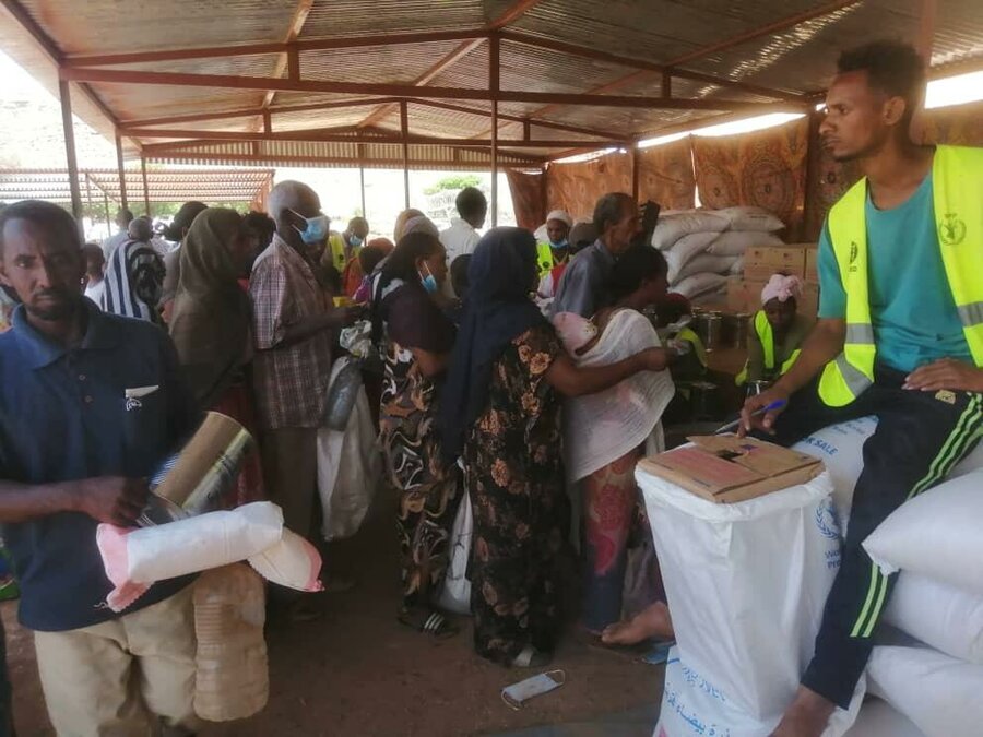 man in wfp high visibility vest distributes food to a crowd in Sudan