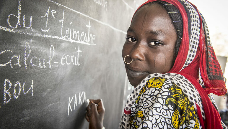 Kaka Marabou kirjoittamassa nimeään koulun taululle Yakoualla, Tšad-järvellä. Pakolaiset, asuinsijoiltaan siirtymään joutuneet ihmiset ja muut köyhät yhteisöt Tšad-järven vesistöalueella ovat riippuvaisia humanitaarisesta avusta selviytymisensä turvaamiseksi. Myös peruskoulutuksen saanti on rajallista. WFP/Giulio d'Adamo.